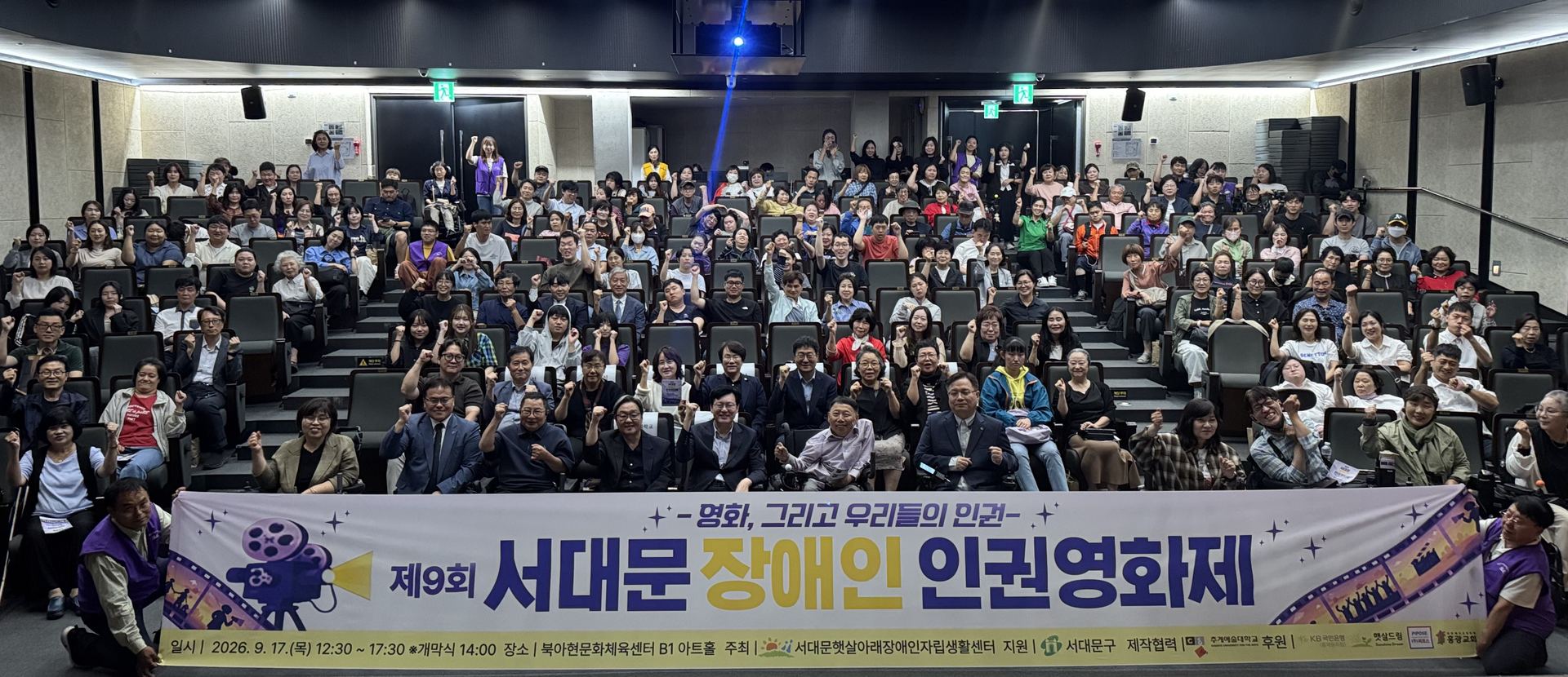 제9회 서대문 장애인 인권영화제(2026년 9월 17일, 북아현 문화체육센터). 객석을 가득 채운 관객들이 손을 들어 인사하고, 앞줄에 영화제 현수막이 펼쳐져 있다.